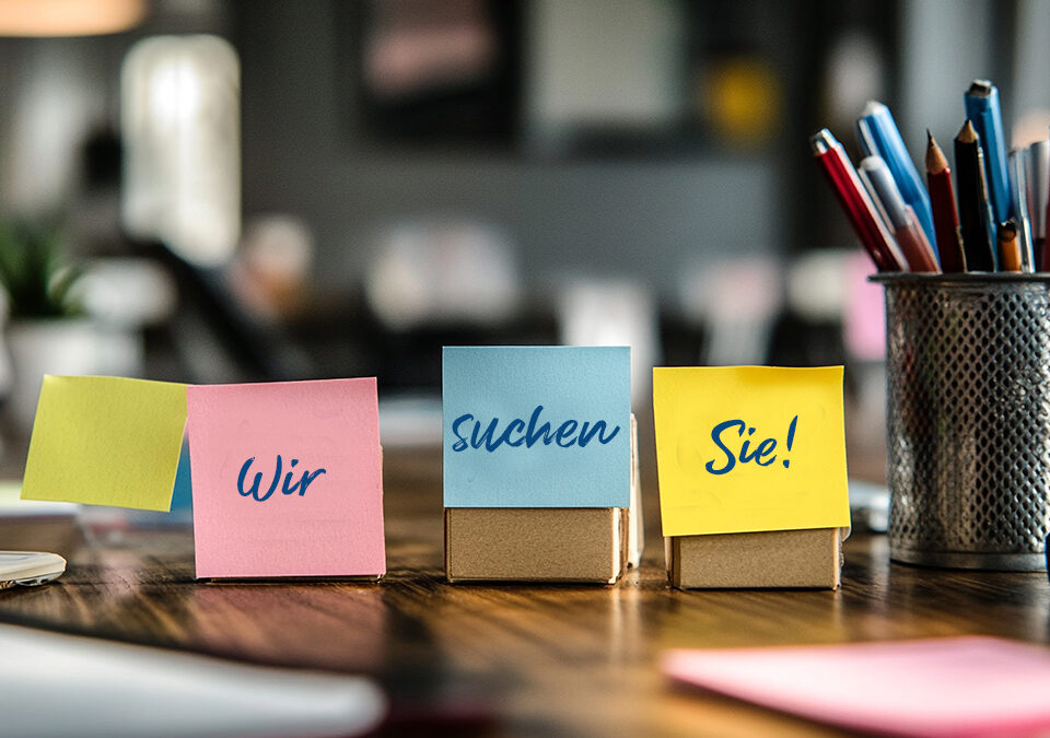 Auf dem Bild sieht man einen Schreibtisch mit drei Postits auf denen Wir suchen Sie steht.